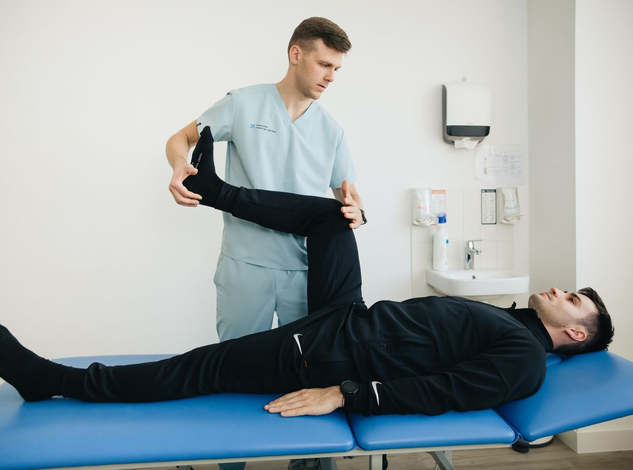 physiotherapist assists patient leg stretching on treatment table