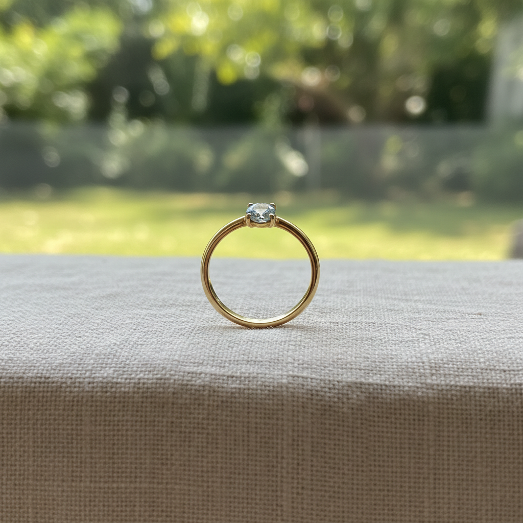 A gold ring set with a single small pale stone standing upright on linen, soft daylight, close crop, no people, no text, no signage